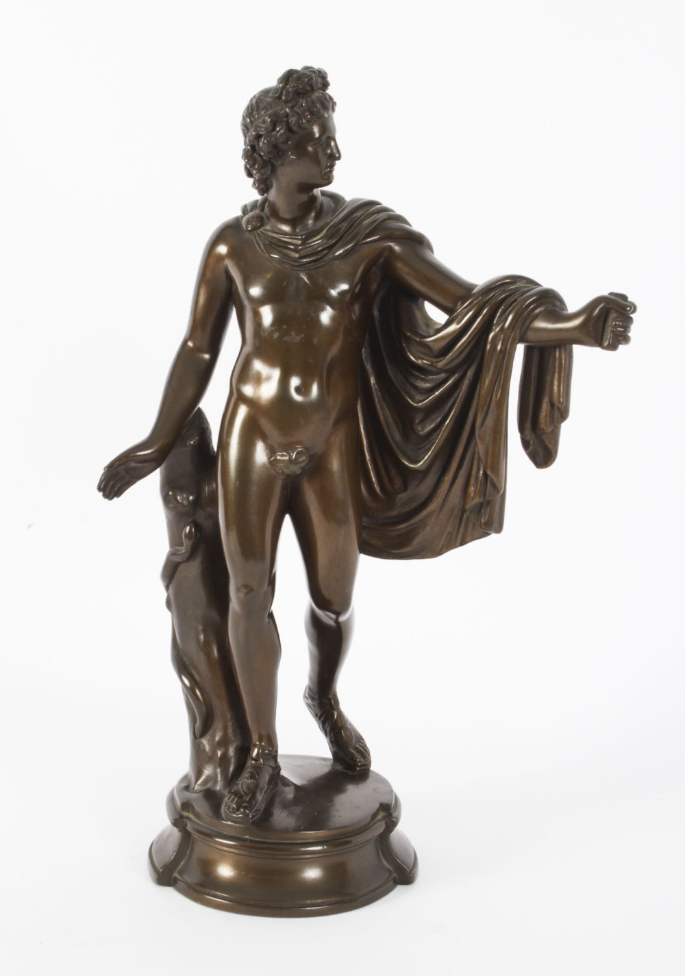 A nineteenth-century dark brown bronze sculpture depicting the classical Greek god Apollo standing with draped cloth on a circular base.