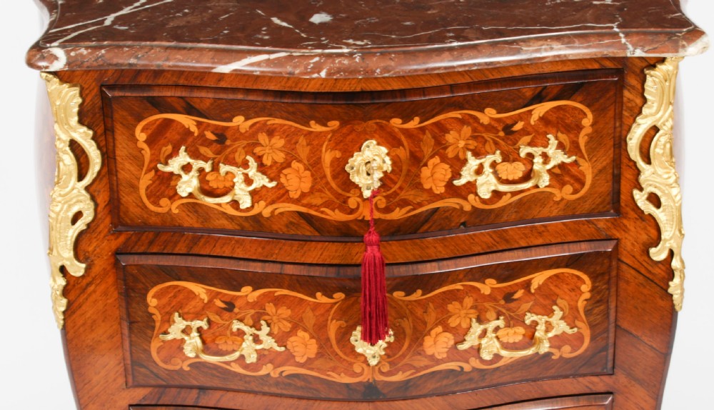 A French Louis XV Revival style marquetry commode featuring floral timber inlays, gilt-bronze mounts, three drawers, and a contoured marble top. View VI