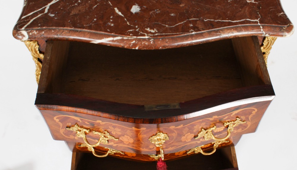 A French Louis XV Revival style marquetry commode featuring floral timber inlays, gilt-bronze mounts, three drawers, and a contoured marble top. View XV