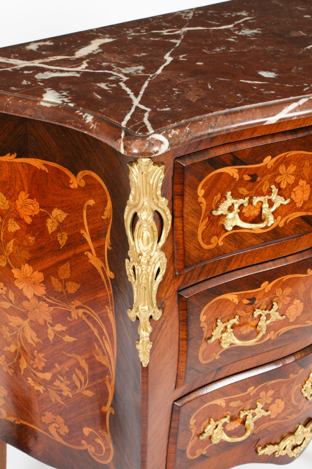 A French Louis XV Revival style marquetry commode featuring floral timber inlays, gilt-bronze mounts, three drawers, and a contoured marble top. View XVI