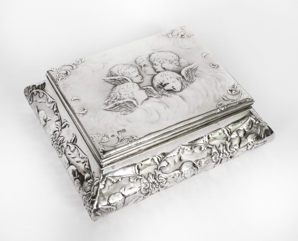 A rectangular sterling silver casket featuring relief repousse cherub heads on the hinged lid and scrollwork along the flared base.