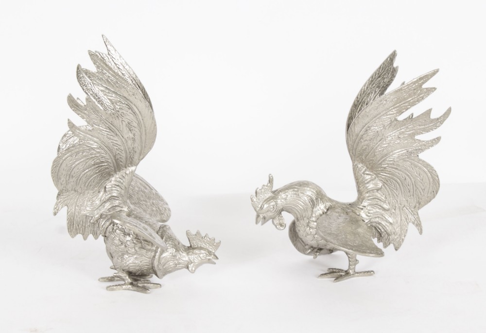 A pair of silver-plated fighting cockerels facing each other in dynamic poses with detailed plumage.