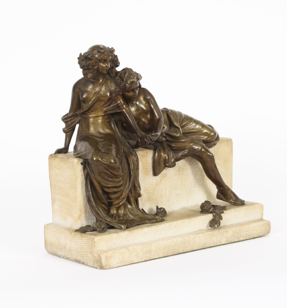A dark bronze sculpture depicting two classical draped figures resting on a light-coloured carved marble bench base.