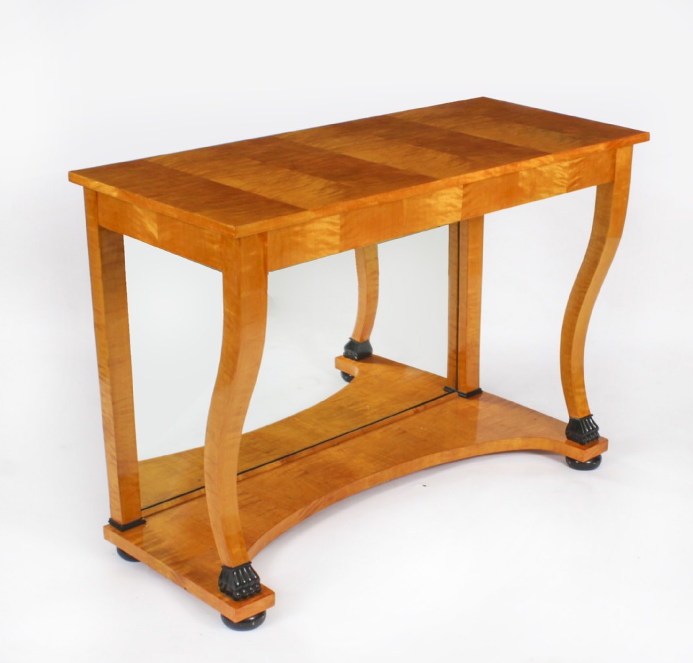 A 19th-century Biedermeier console table featuring figured maserbirch veneer, a mirrored back panel, curved front legs with ebonised feet, and a concave lower shelf.