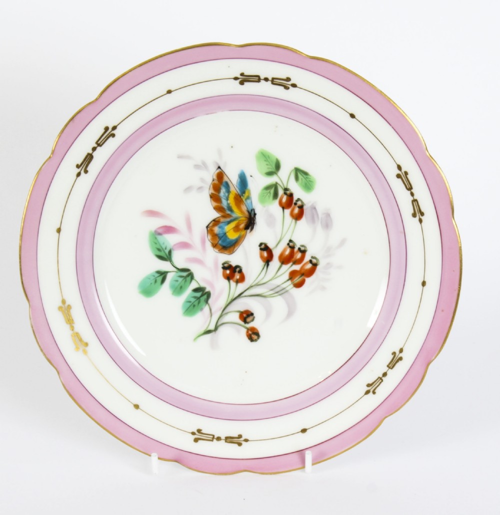 An antique French porcelain cabinet plate featuring a scalloped pink border with gilded accents and a central hand-painted motif of a butterfly and wild berries.