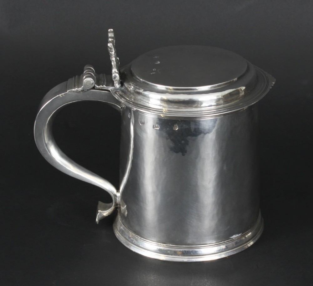 A seventeenth-century sterling silver lidded tankard featuring a tapered cylindrical body, a scroll handle with a hinged thumbpiece, and visible hallmarks.