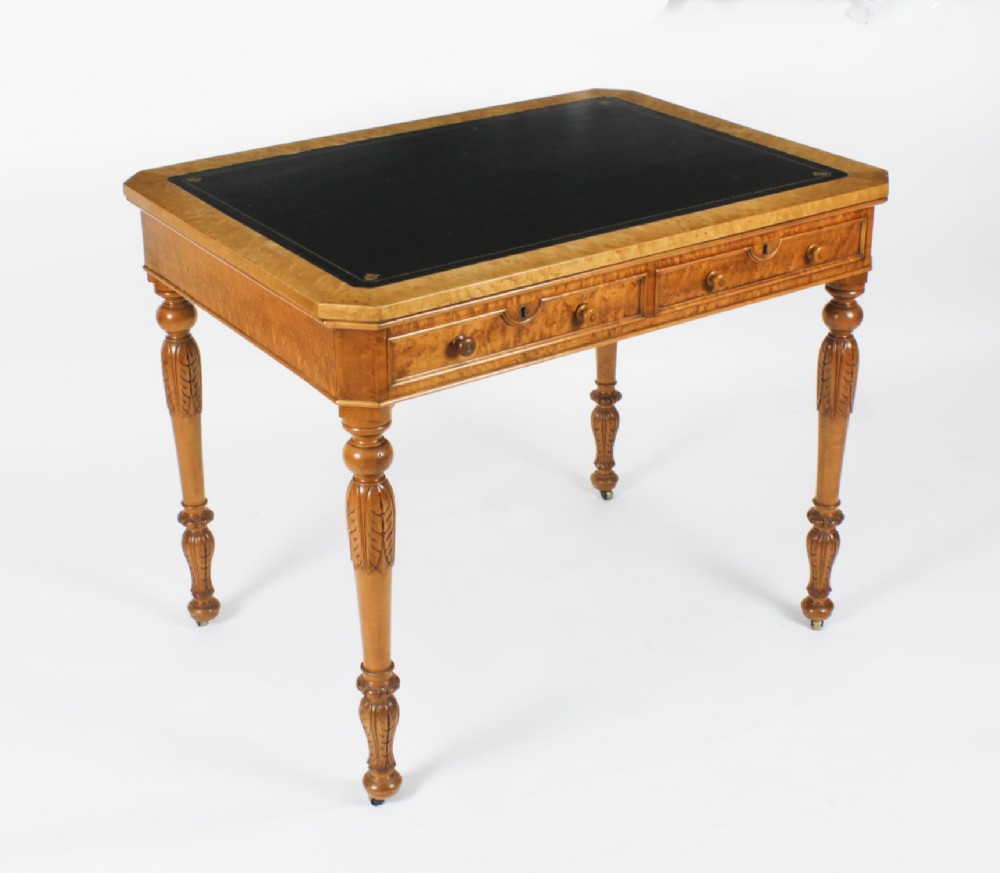 A late 19th-century birdseye maple writing table featuring a black leather inset top, two front frieze drawers, and turned carved legs on brass castors.