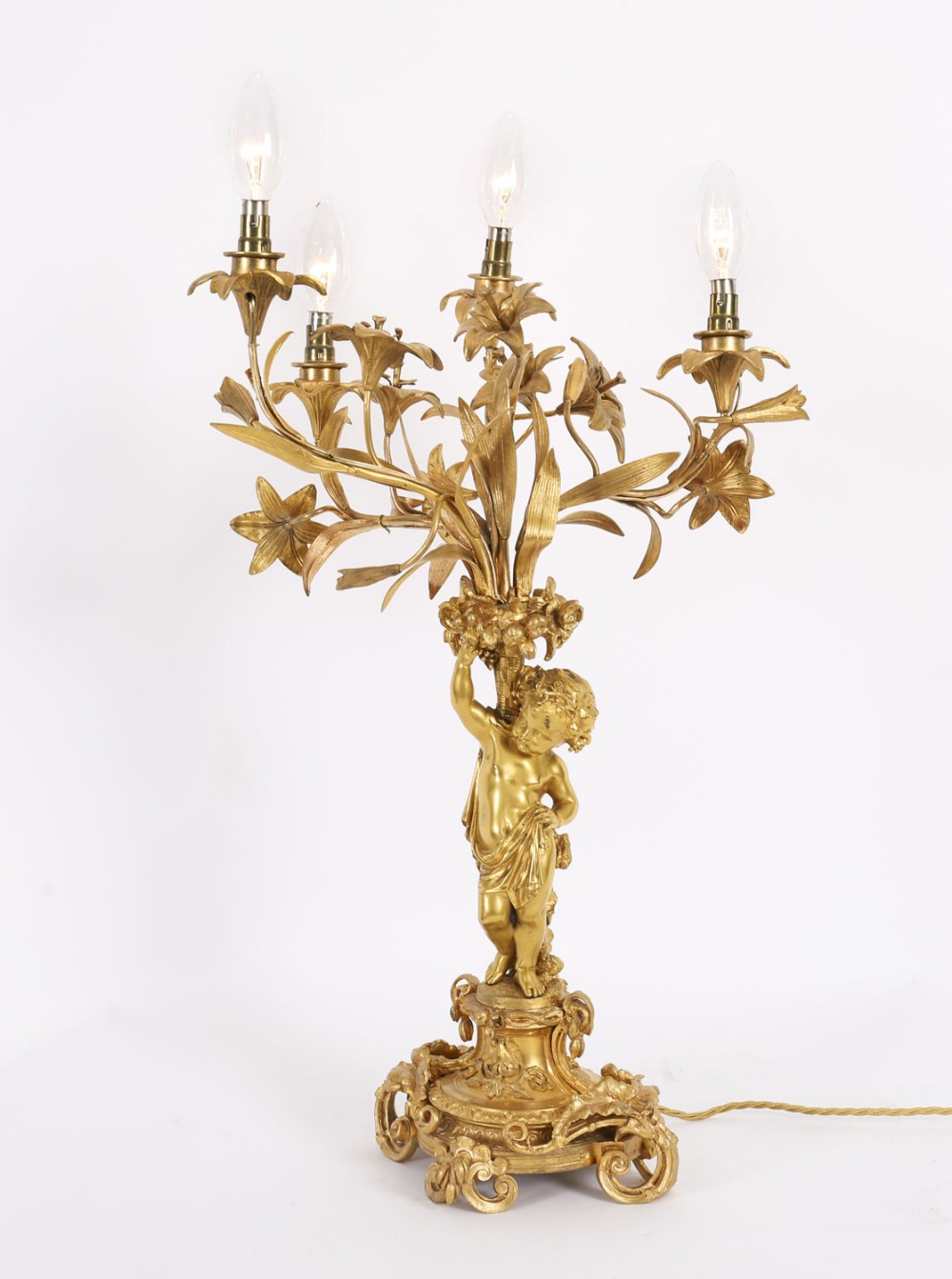 A French gilt bronze table lamp featuring a sculpted cherub holding lily-shaped light sockets on a Rococo scrolled base.