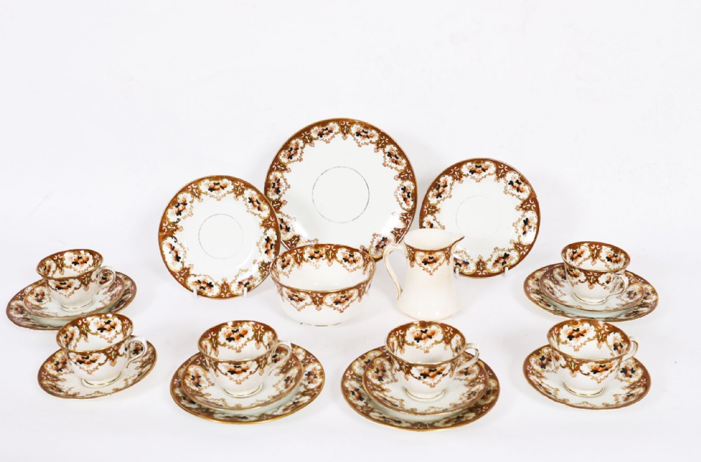 An antique twenty-one piece bone china tea set featuring white porcelain decorated with elaborate brown and gilded floral border patterns.