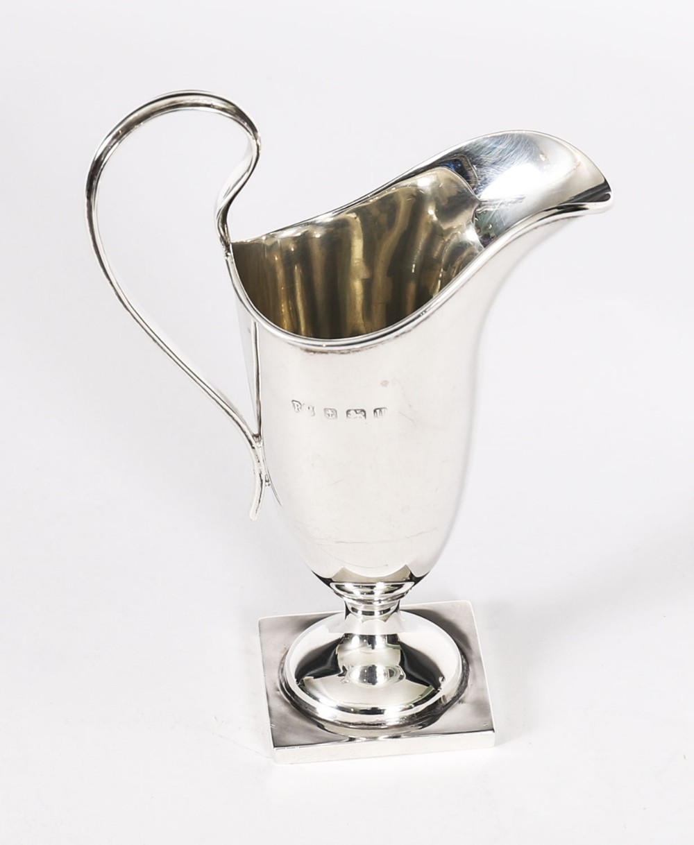 A solid sterling silver cream jug featuring a high loop handle, flared spout, and a square pedestal base.