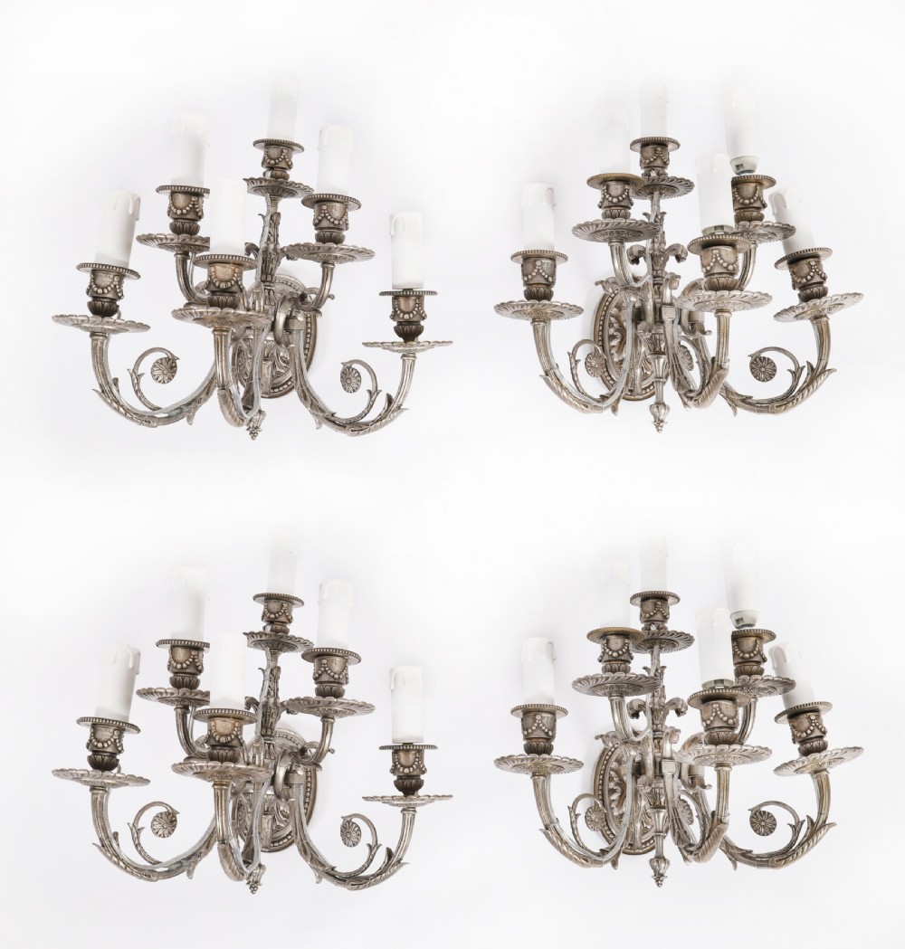 A set of four silver-plated six-branch wall sconces featuring scrolling arms, foliate details, and faux candle sleeves.