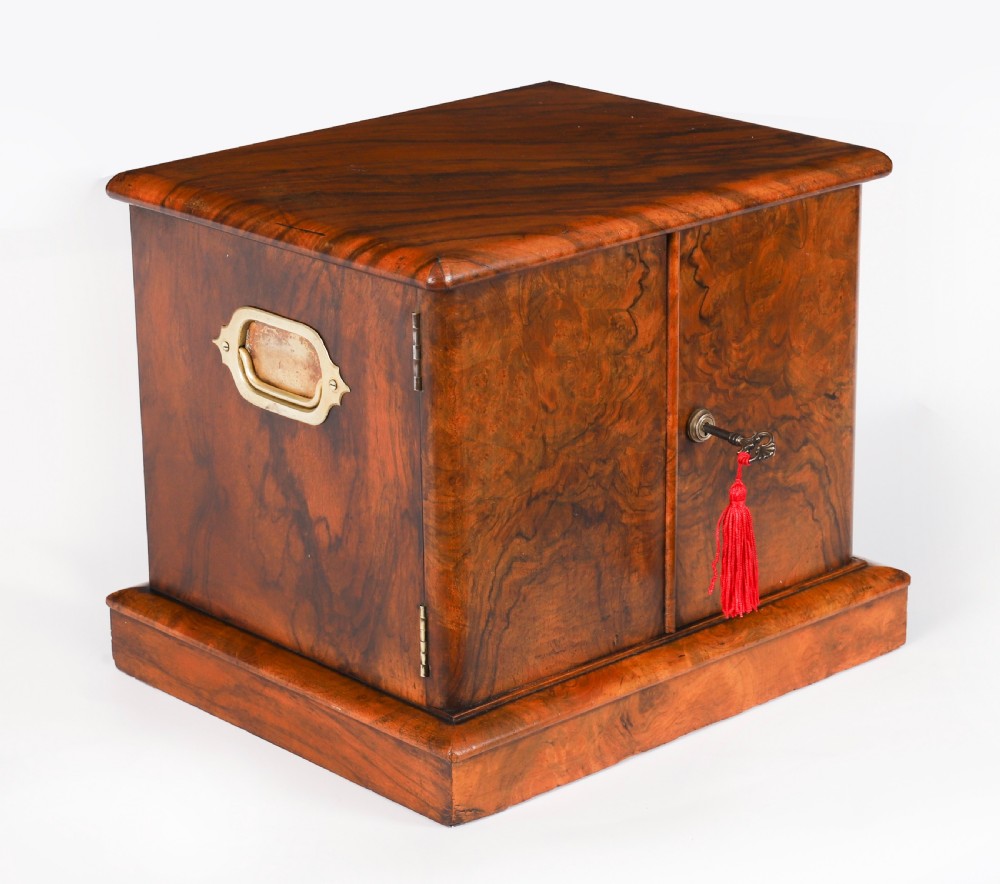A Victorian burr walnut desktop cigar cabinet featuring brass campaign carry handles, twin doors, a moulded plinth base, and a key with a red tassel.