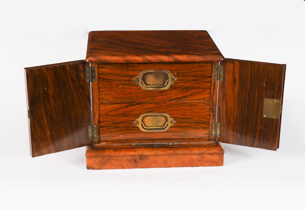 A Victorian burr walnut desktop cigar cabinet featuring brass campaign carry handles, twin doors, a moulded plinth base, and a key with a red tassel. View II