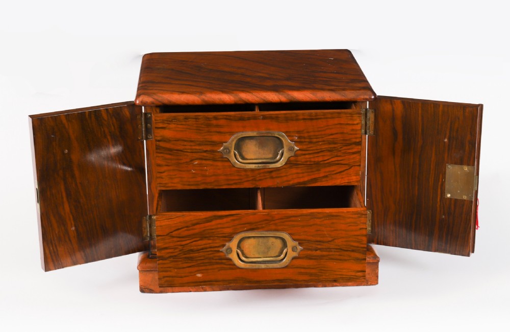 A Victorian burr walnut desktop cigar cabinet featuring brass campaign carry handles, twin doors, a moulded plinth base, and a key with a red tassel. View III