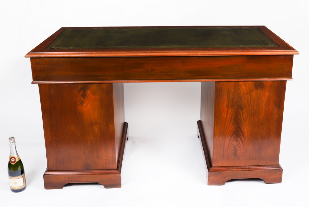 A Victorian flame mahogany pedestal desk featuring a green leather inset writing surface, crossbanded drawers with brass swan-neck handles, and plinth bases. View XV