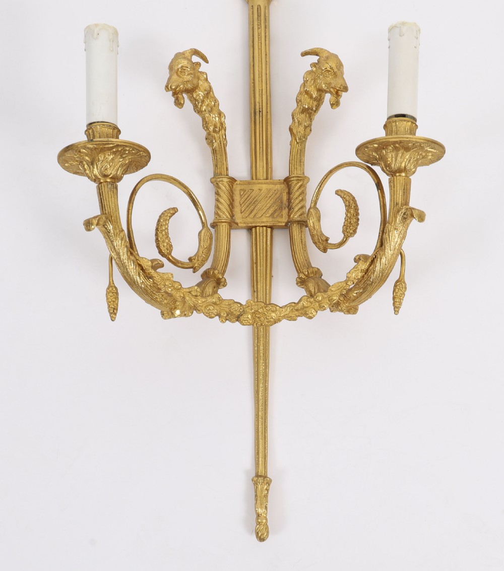 A pair of nineteenth-century French Neoclassical gilt bronze wall lights featuring twin candle arms decorated with goat heads and pinecone finials. View V