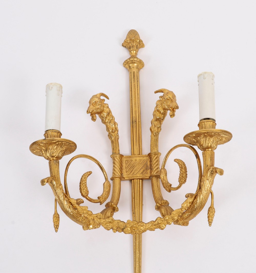 A pair of nineteenth-century French Neoclassical gilt bronze wall lights featuring twin candle arms decorated with goat heads and pinecone finials. View VI