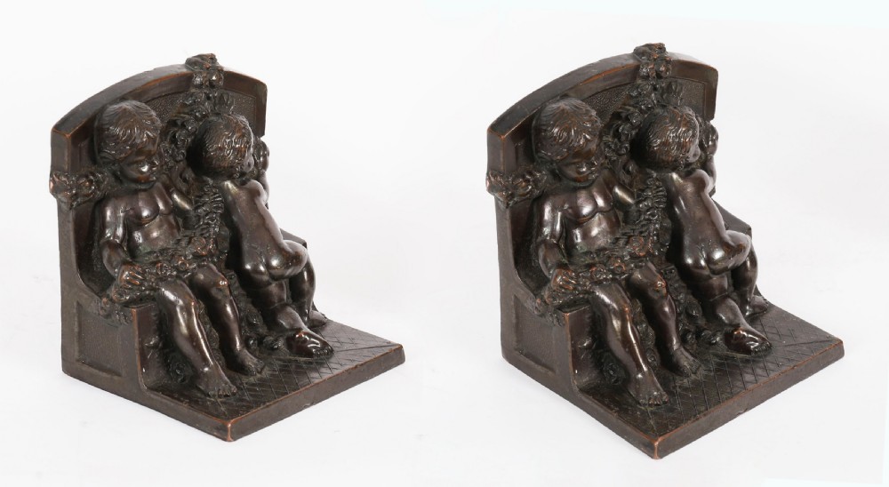 A pair of dark brown patinated bronze bookends depicting seated classical cherubs holding floral garlands on stepped bases.