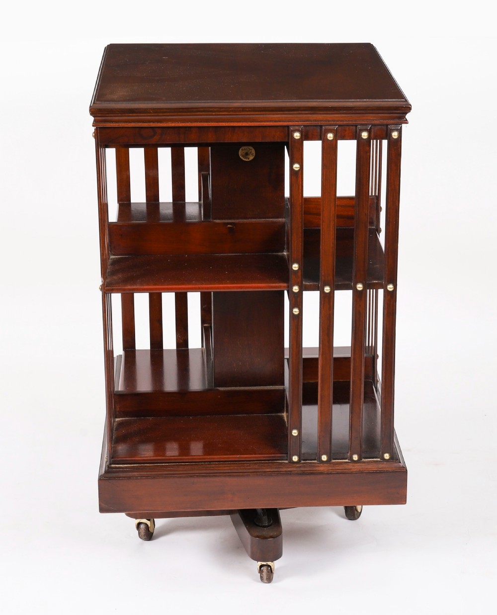A two-tier dark mahogany revolving bookcase featuring vertical slatted sides with brass stud detailing, resting on a quadform base with castors. View IV