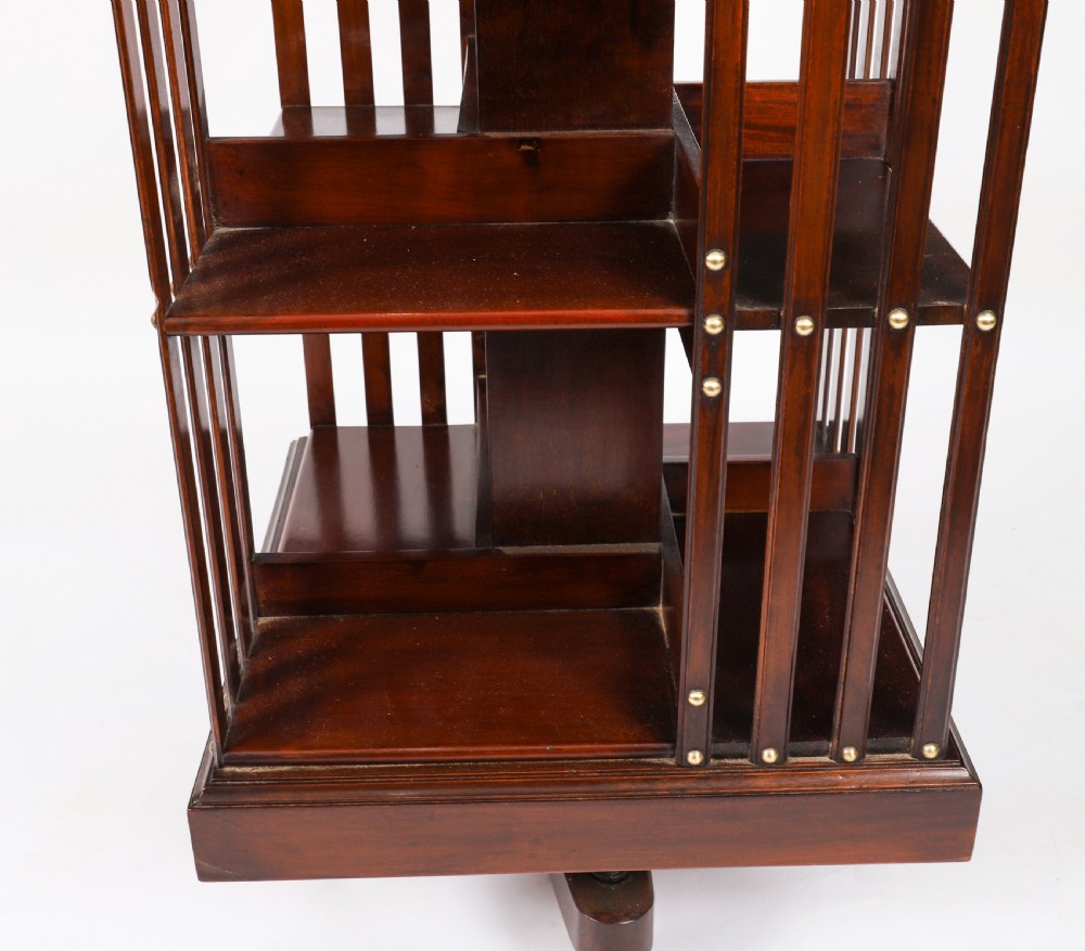 A two-tier dark mahogany revolving bookcase featuring vertical slatted sides with brass stud detailing, resting on a quadform base with castors. View V