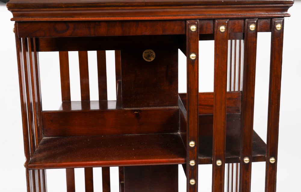 A two-tier dark mahogany revolving bookcase featuring vertical slatted sides with brass stud detailing, resting on a quadform base with castors. View VII