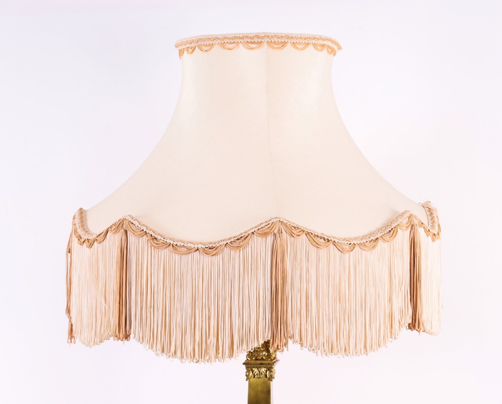 A pair of 19th-century French ormolu table lamps featuring cast gilt bronze bases and cream flared fabric shades with tassel fringe trim. View V