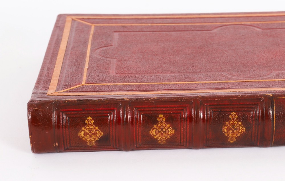 An open red marbled book-form box displaying seven oval cream plaster intaglios behind glass alongside an engraved frontispiece. View V