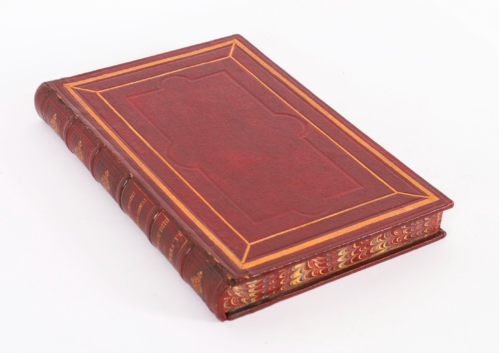 An open red marbled book-form box displaying seven oval cream plaster intaglios behind glass alongside an engraved frontispiece. View VII