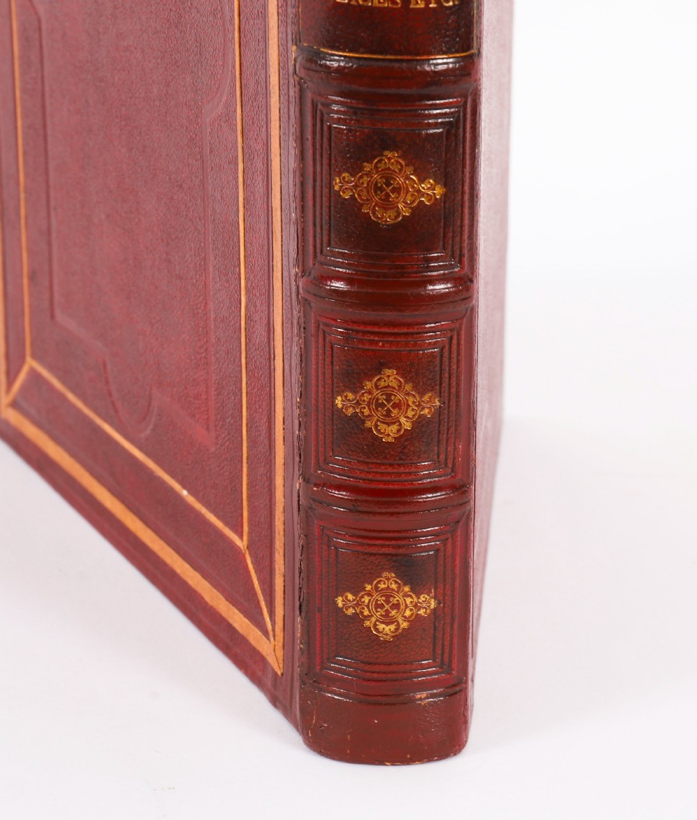 An open red marbled book-form box displaying seven oval cream plaster intaglios behind glass alongside an engraved frontispiece. View XII