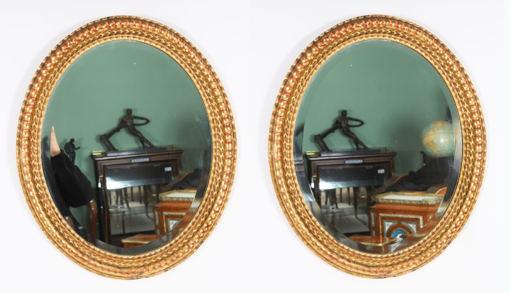 A matching pair of 19th-century French oval wall mirrors featuring carved giltwood frames with a beaded pattern and gold leaf finish.
