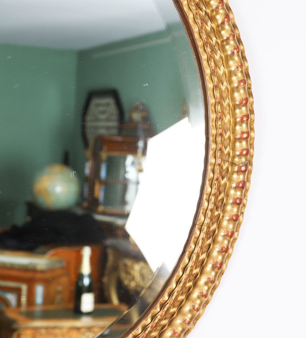A matching pair of 19th-century French oval wall mirrors featuring carved giltwood frames with a beaded pattern and gold leaf finish. View III