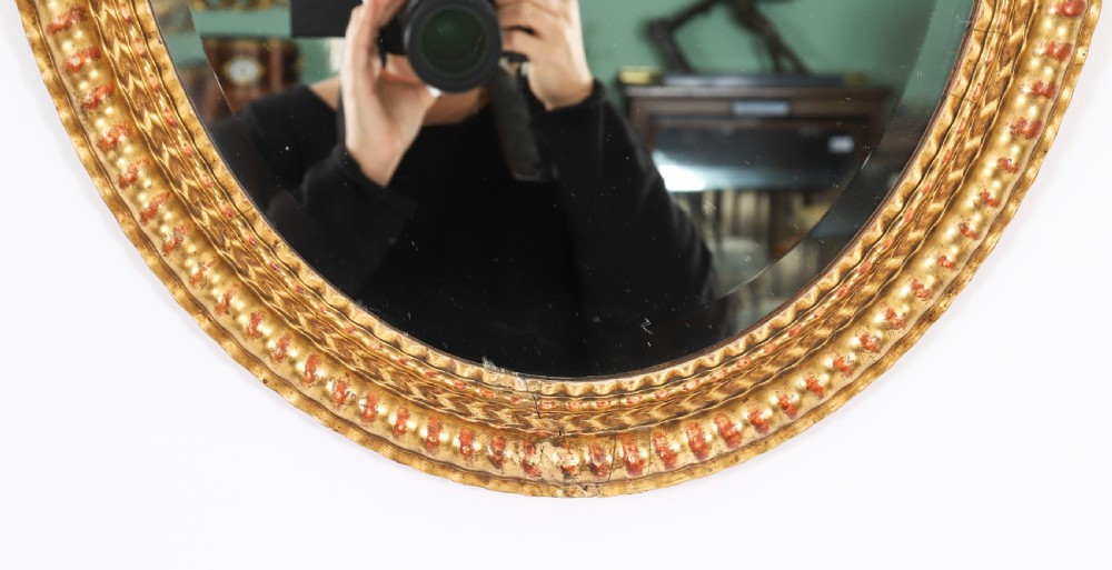 A matching pair of 19th-century French oval wall mirrors featuring carved giltwood frames with a beaded pattern and gold leaf finish. View IV