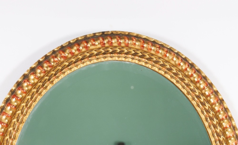 A matching pair of 19th-century French oval wall mirrors featuring carved giltwood frames with a beaded pattern and gold leaf finish. View V