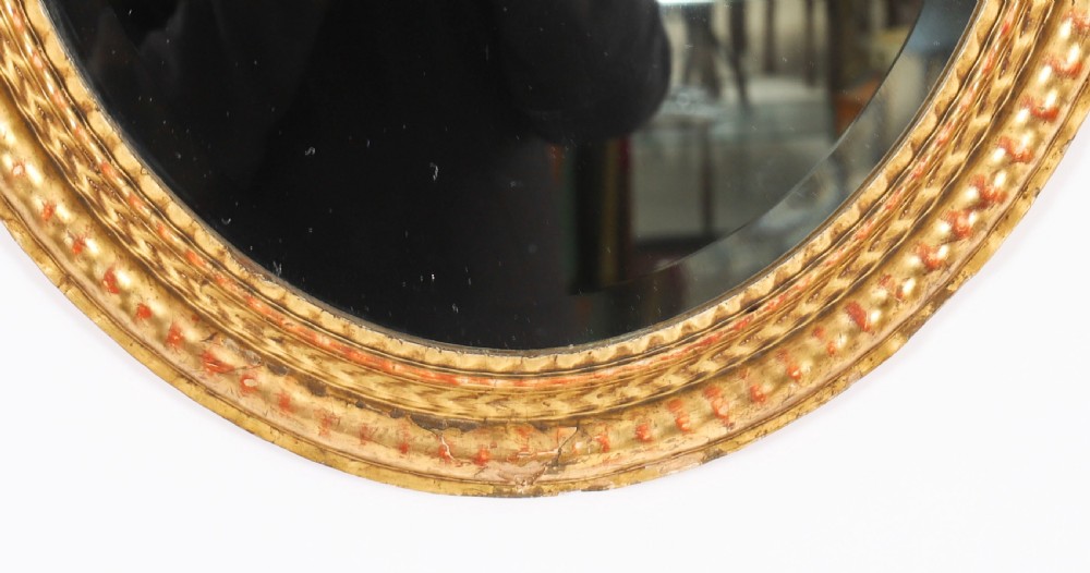 A matching pair of 19th-century French oval wall mirrors featuring carved giltwood frames with a beaded pattern and gold leaf finish. View X