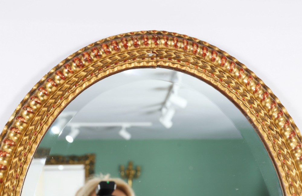 A matching pair of 19th-century French oval wall mirrors featuring carved giltwood frames with a beaded pattern and gold leaf finish. View XII