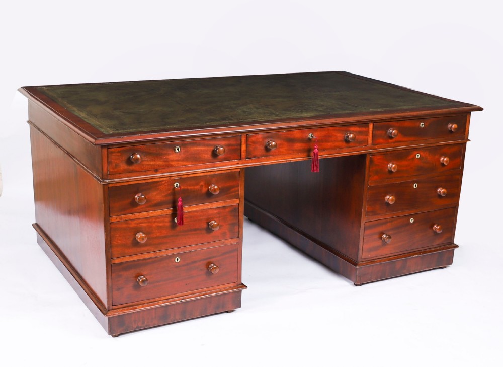 A Victorian flame mahogany partners pedestal desk featuring a green leather inset writing surface and turned wooden knobs.