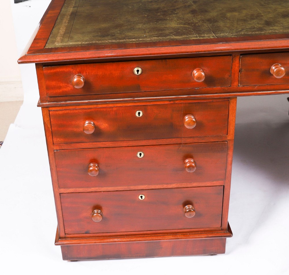 A Victorian flame mahogany partners pedestal desk featuring a green leather inset writing surface and turned wooden knobs. View X