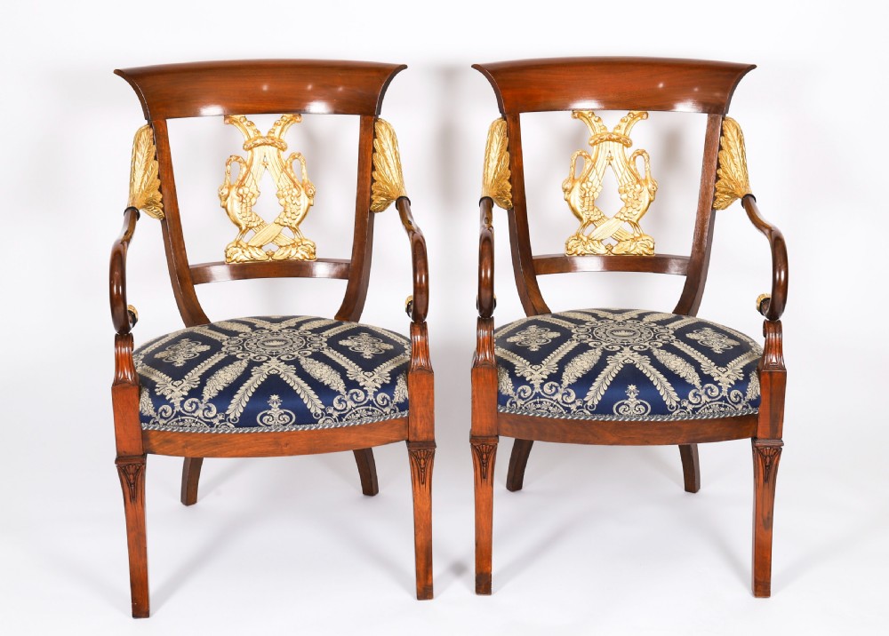 A pair of Italian Neoclassical armchairs featuring dark wood frames with giltwood swan carved back splats and blue patterned upholstered seats.