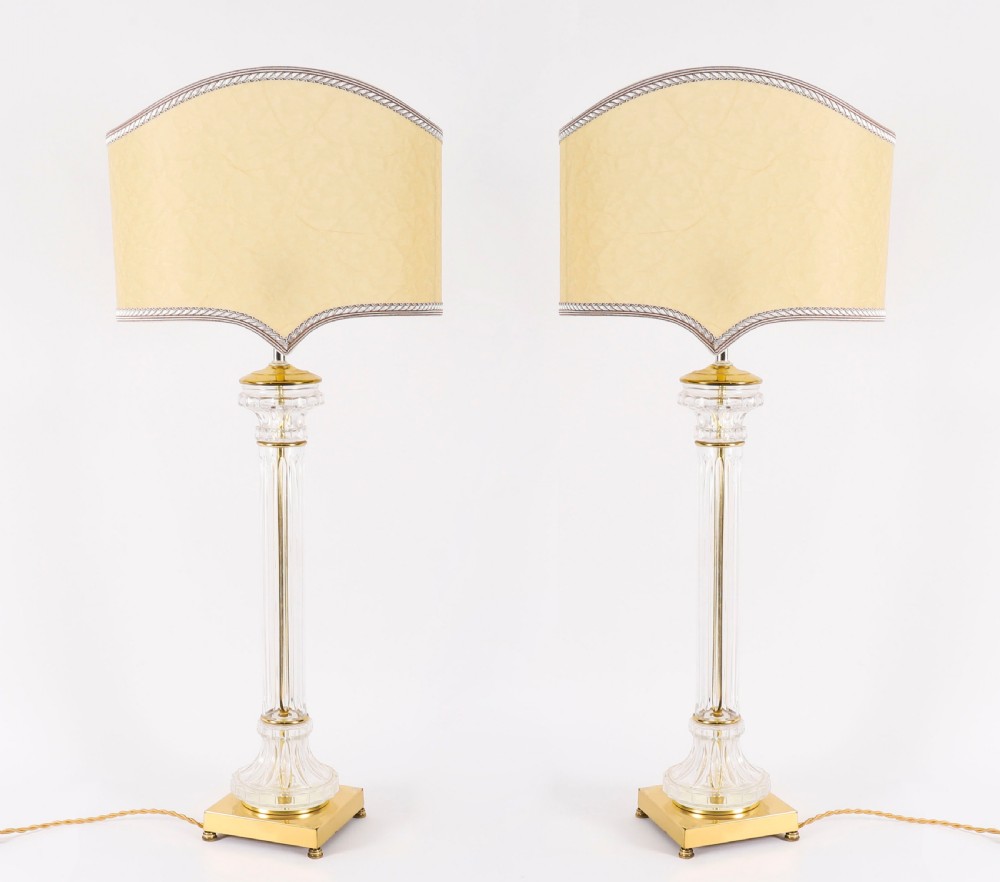 A pair of Art Deco table lamps featuring fluted clear glass column stems on square gilded metal bases with arched cream lampshades.