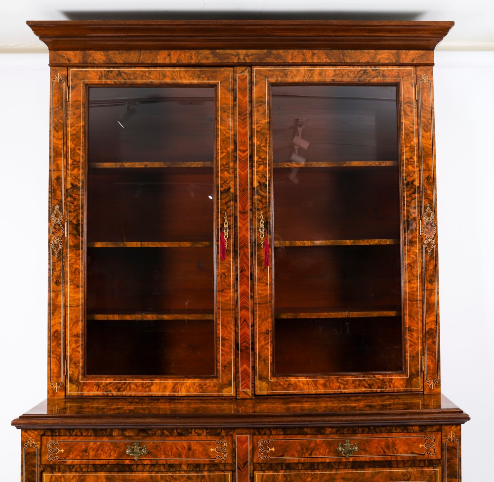 A 19th-century Victorian burr walnut bookcase featuring upper glazed doors, intricate inlay detailing, two drawers, and lower cupboard doors. View III
