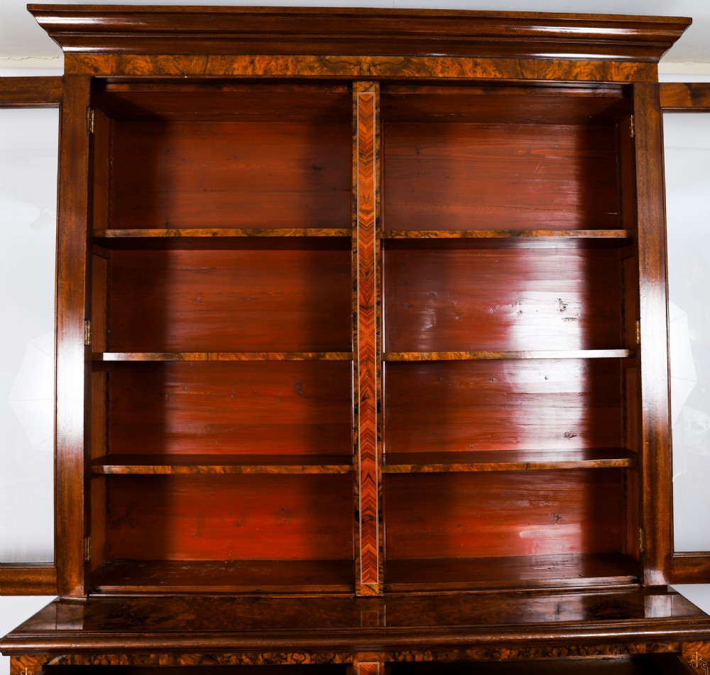 A 19th-century Victorian burr walnut bookcase featuring upper glazed doors, intricate inlay detailing, two drawers, and lower cupboard doors. View V