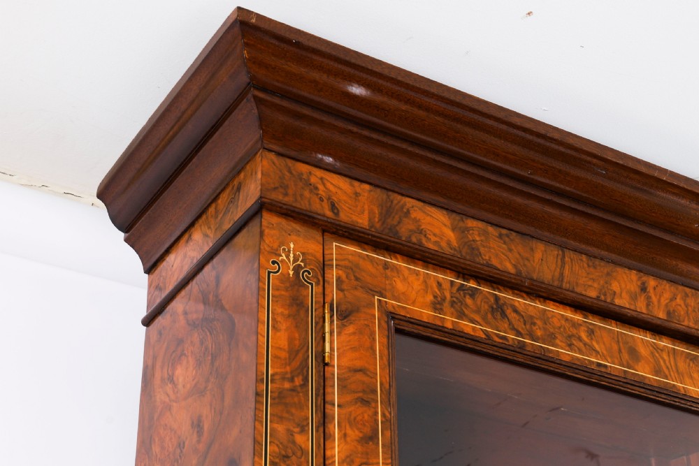 A 19th-century Victorian burr walnut bookcase featuring upper glazed doors, intricate inlay detailing, two drawers, and lower cupboard doors. View VI