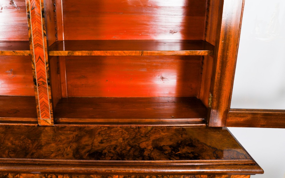 A 19th-century Victorian burr walnut bookcase featuring upper glazed doors, intricate inlay detailing, two drawers, and lower cupboard doors. View VII
