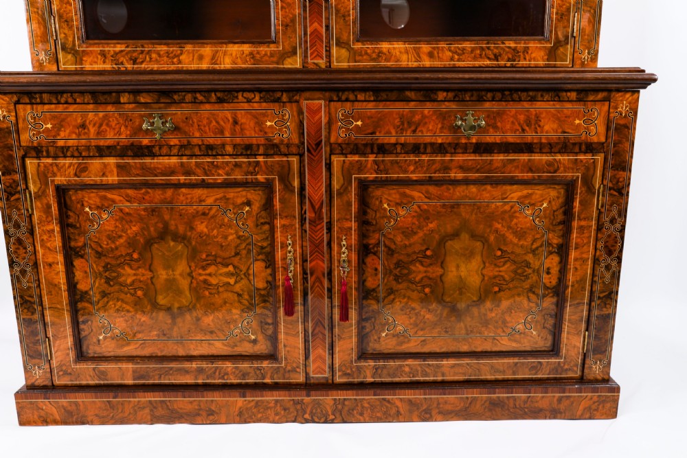 A 19th-century Victorian burr walnut bookcase featuring upper glazed doors, intricate inlay detailing, two drawers, and lower cupboard doors. View X