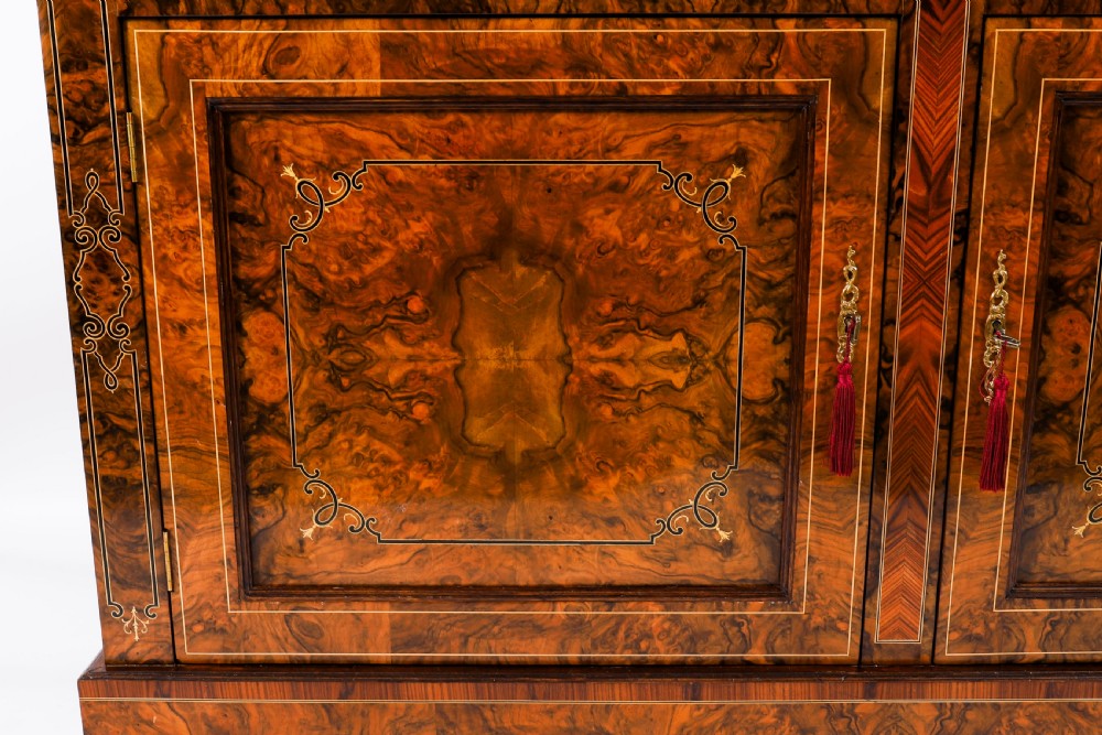 A 19th-century Victorian burr walnut bookcase featuring upper glazed doors, intricate inlay detailing, two drawers, and lower cupboard doors. View XI
