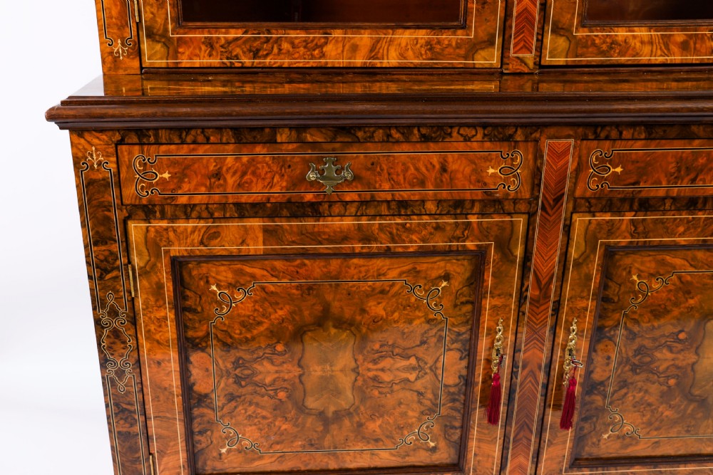 A 19th-century Victorian burr walnut bookcase featuring upper glazed doors, intricate inlay detailing, two drawers, and lower cupboard doors. View XII