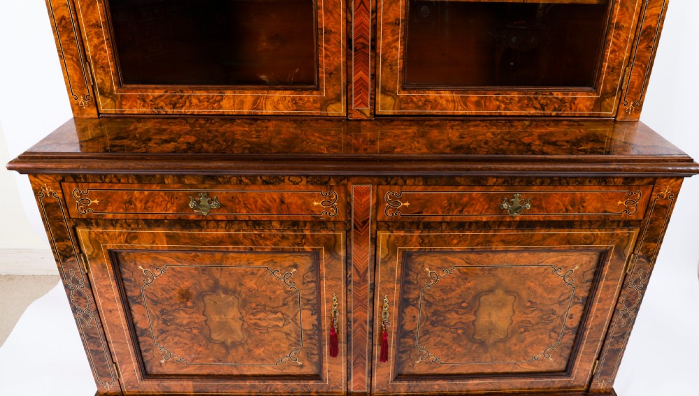 A 19th-century Victorian burr walnut bookcase featuring upper glazed doors, intricate inlay detailing, two drawers, and lower cupboard doors. View XIV