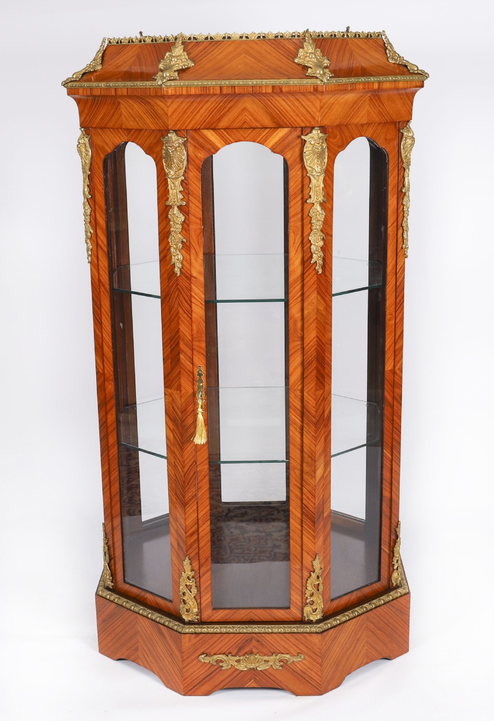 An octagonal kingwood display cabinet featuring chevron parquetry veneers, gilt bronze mounts, and glazed panels housing internal glass shelves.