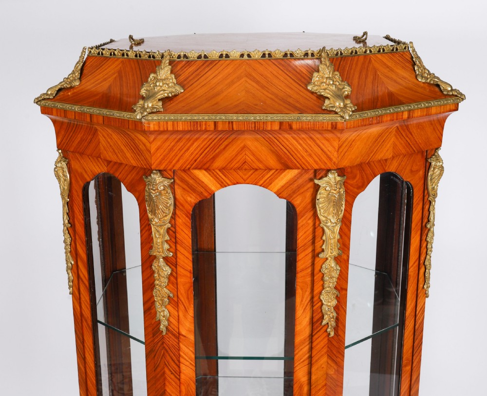 An octagonal kingwood display cabinet featuring chevron parquetry veneers, gilt bronze mounts, and glazed panels housing internal glass shelves. View IV