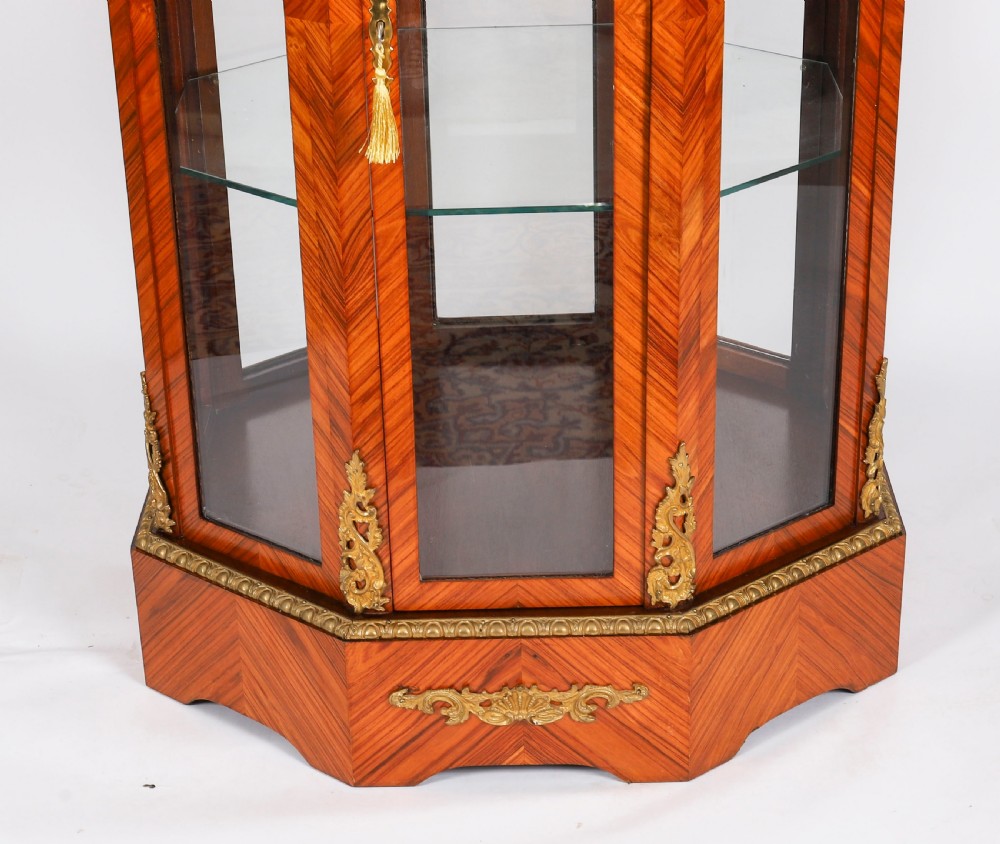 An octagonal kingwood display cabinet featuring chevron parquetry veneers, gilt bronze mounts, and glazed panels housing internal glass shelves. View V